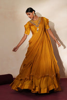 Woman in a golden yellow traditional outfit standing againsta beige wall on a red carpet.