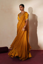 Woman in a golden yellow traditional outfit standing againsta beige wall on a red carpet.
