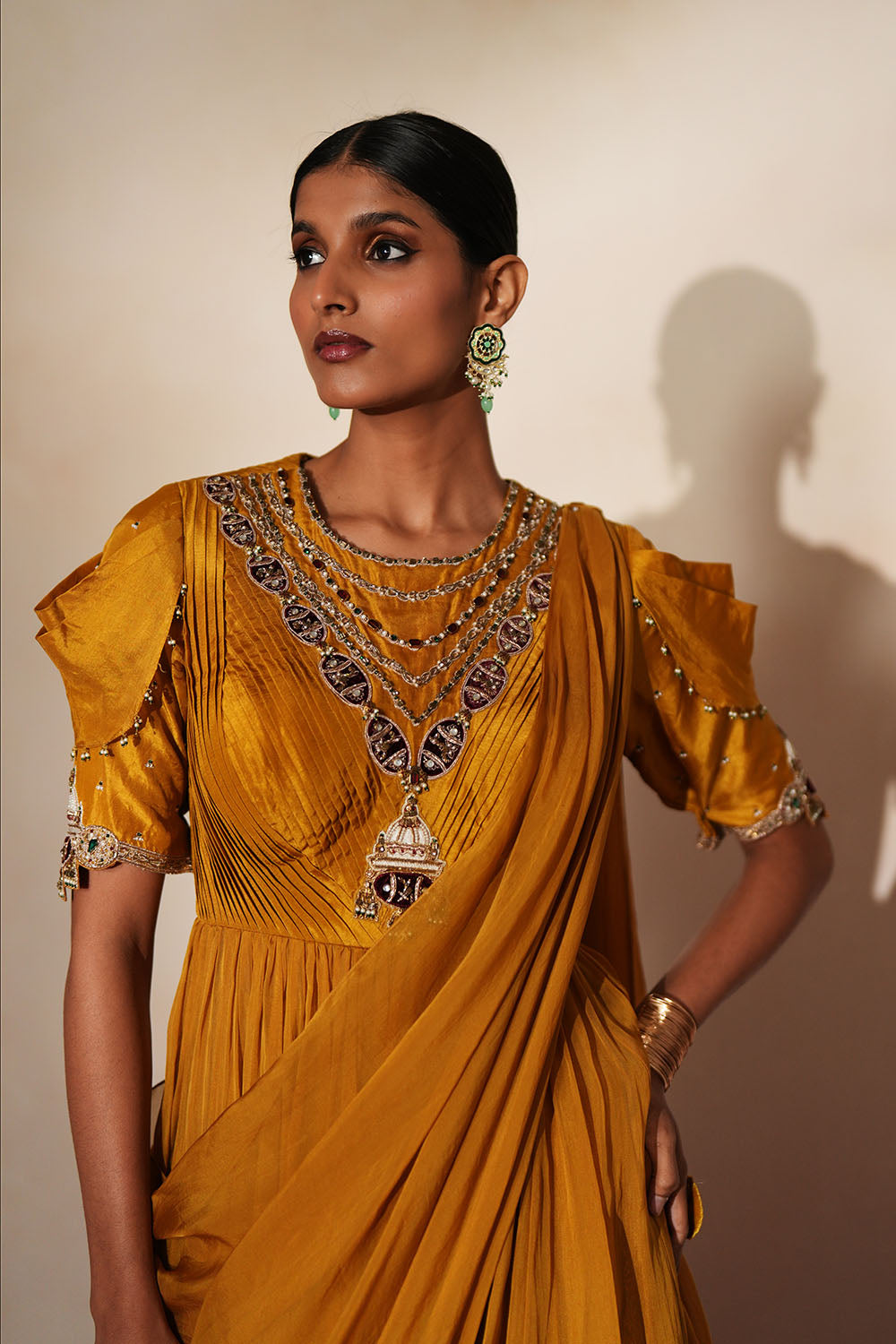 Woman in a golden yellow traditional outfit standing againsta beige wall on a red carpet.