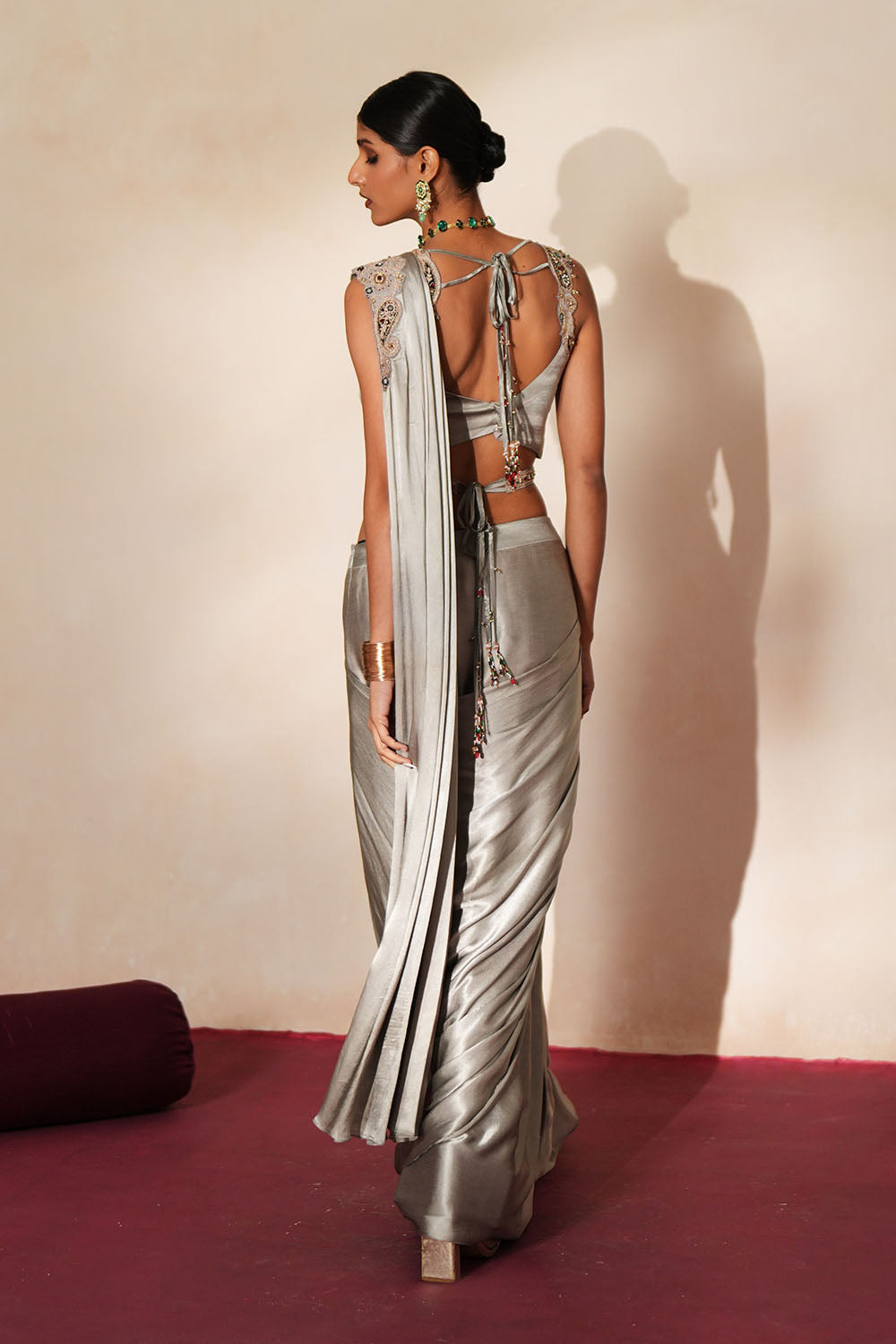 Woman in a mettalic grey traditional outfit standing againsta beige wall on a red carpet.