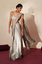 Woman in a mettalic grey traditional outfit standing againsta beige wall on a red carpet.