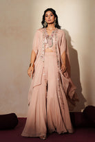 Woman in a soft pink traditional outfit standing againsta beige wall on a red carpet.
