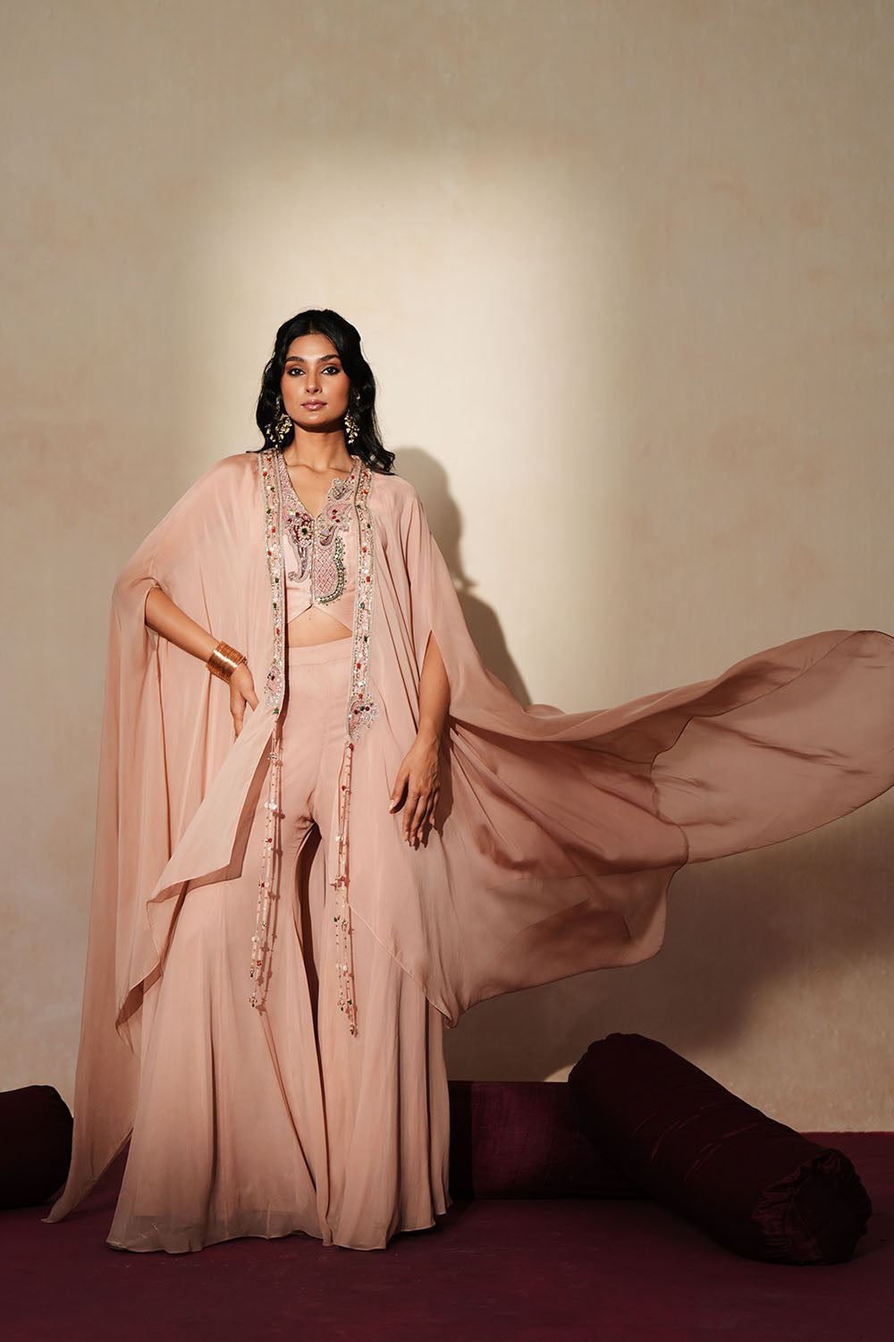 Woman in a soft pink traditional outfit standing againsta beige wall on a red carpet.