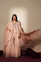 Woman in a soft pink traditional outfit standing againsta beige wall on a red carpet.