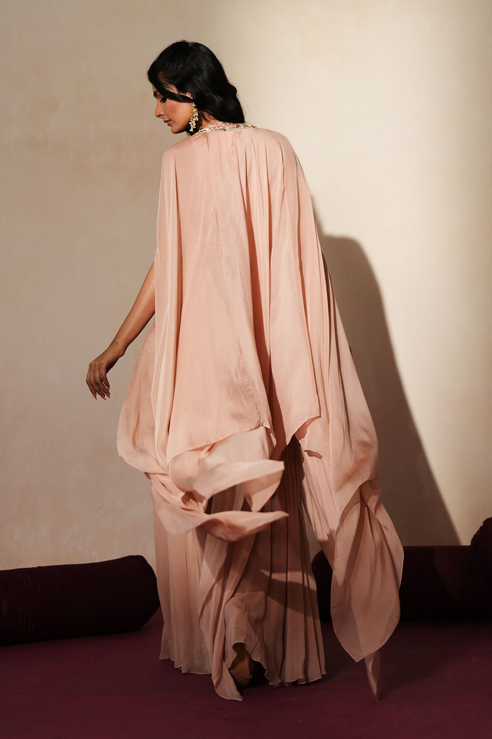 Woman in a soft pink traditional outfit standing againsta beige wall on a red carpet.