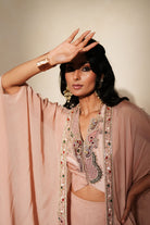 Woman in a soft pink traditional outfit standing againsta beige wall on a red carpet.
