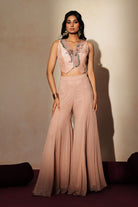 Woman in a soft pink traditional outfit standing againsta beige wall on a red carpet.