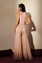 Woman in a soft pink traditional outfit standing againsta beige wall on a red carpet.