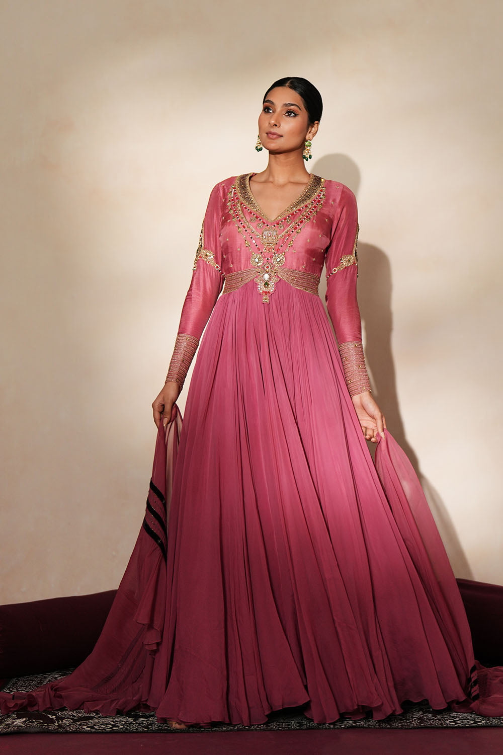 Woman in a mauve pink traditional outfit standing againsta beige wall on a red carpet.