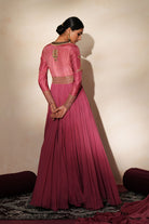 Woman in a mauve pink traditional outfit standing againsta beige wall on a red carpet.