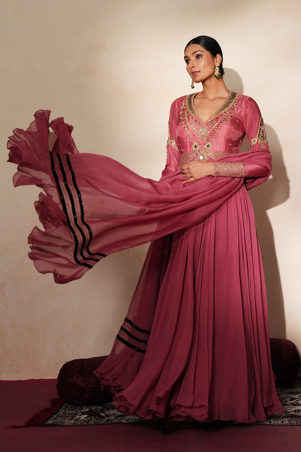 Woman in a mauve pink traditional outfit standing againsta beige wall on a red carpet.