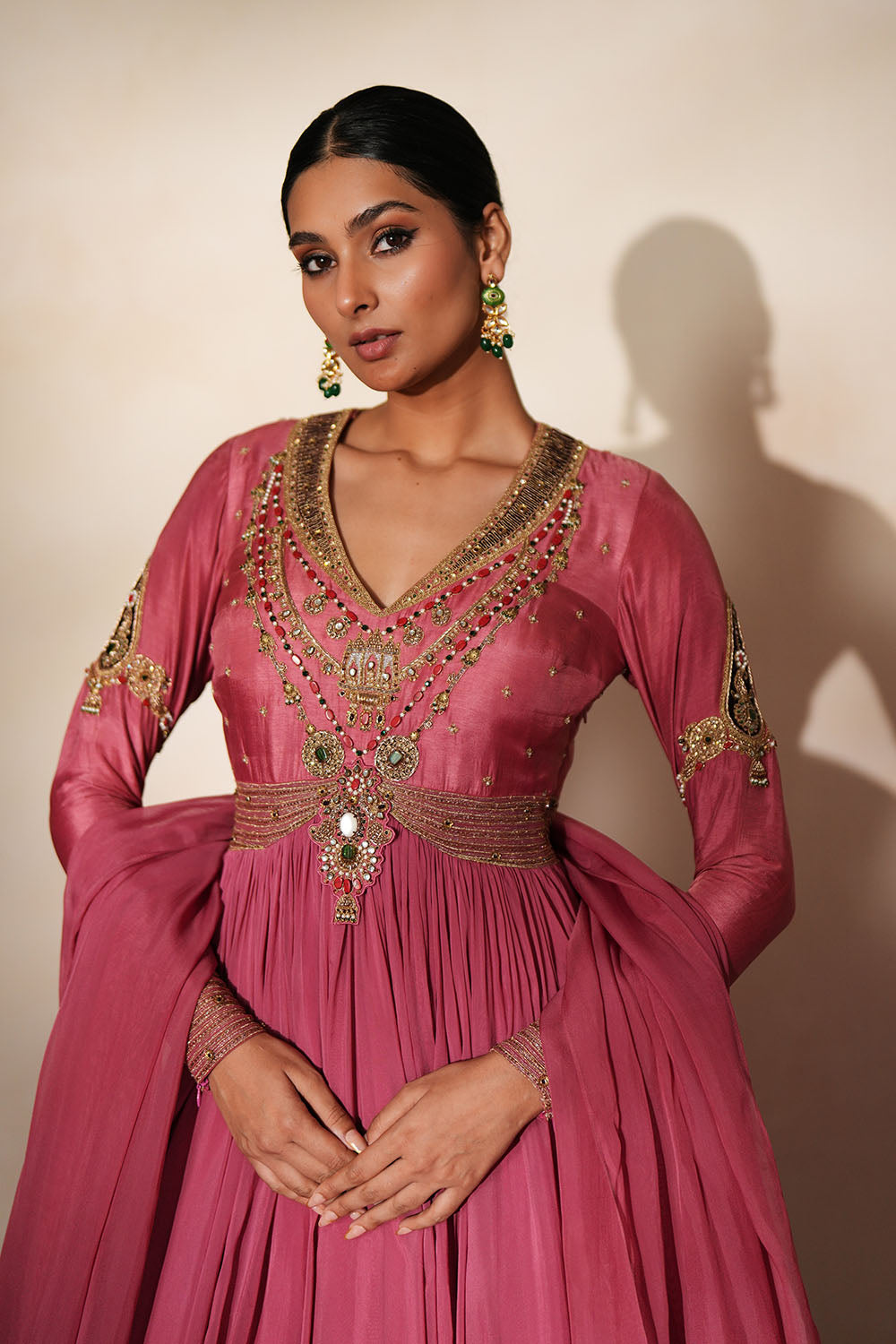 Woman in a mauve pink traditional outfit standing againsta beige wall on a red carpet.