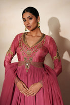 Woman in a mauve pink traditional outfit standing againsta beige wall on a red carpet.