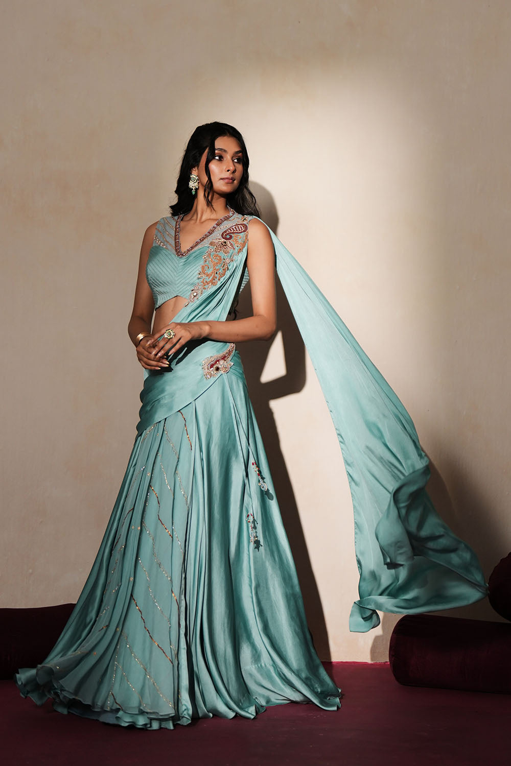 Woman in a pastel blue traditional outfit standing againsta beige wall on a red carpet.