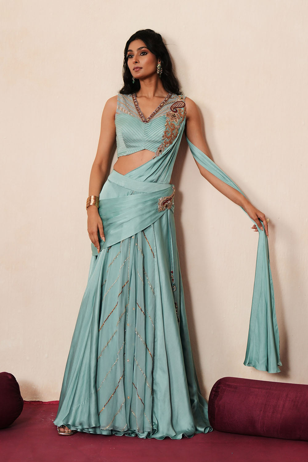 Woman in a pastel blue traditional outfit standing againsta beige wall on a red carpet.