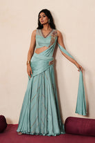 Woman in a pastel blue traditional outfit standing againsta beige wall on a red carpet.