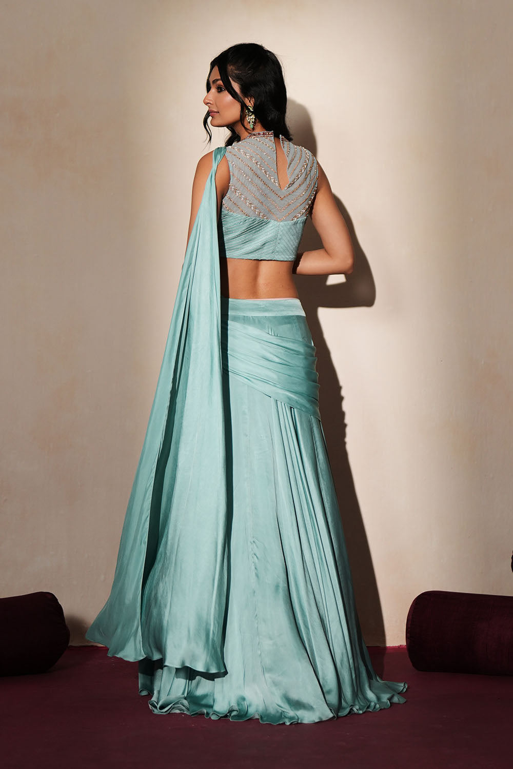 Woman in a pastel blue traditional outfit standing againsta beige wall on a red carpet.