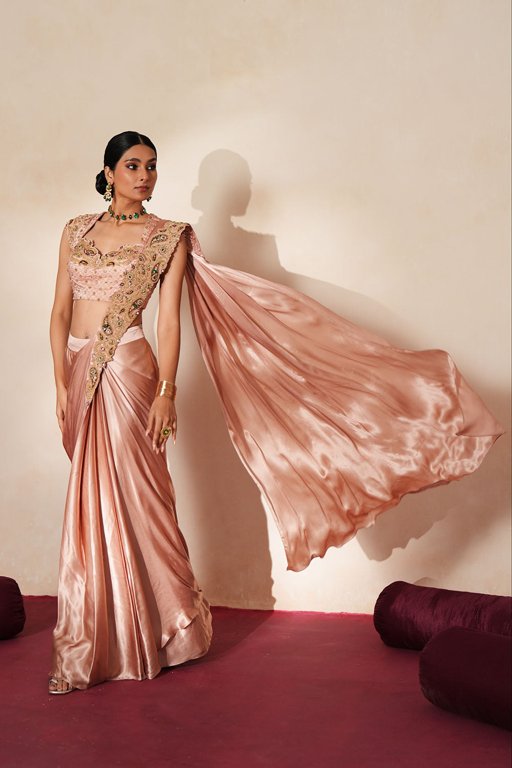 Woman in a soft pink traditional outfit standing againsta beige wall on a red carpet.