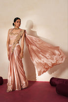 Woman in a soft pink traditional outfit standing againsta beige wall on a red carpet.