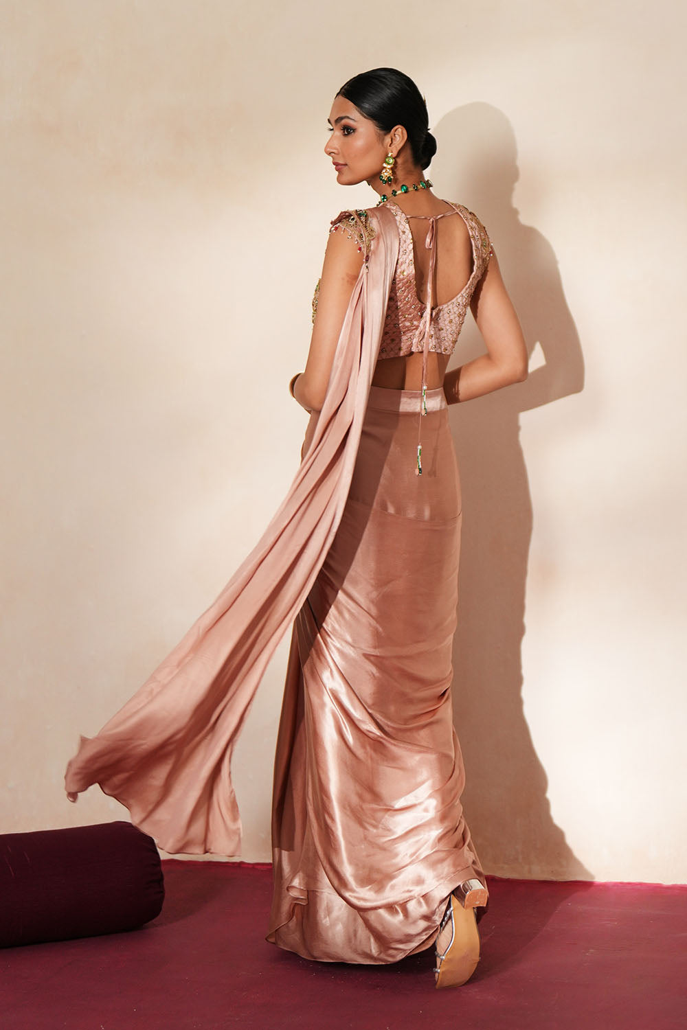 Woman in a soft pink traditional outfit standing againsta beige wall on a red carpet.