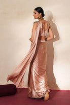 Woman in a soft pink traditional outfit standing againsta beige wall on a red carpet.