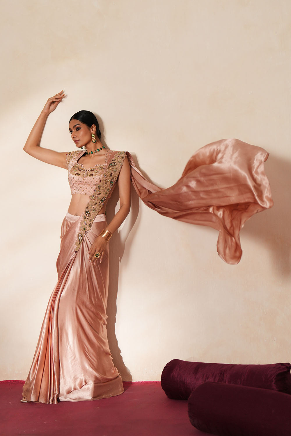 Woman in a soft pink traditional outfit standing againsta beige wall on a red carpet.