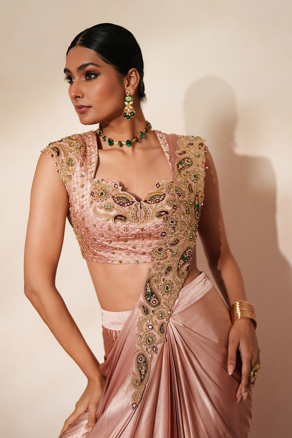 Woman in a soft pink traditional outfit standing againsta beige wall on a red carpet.