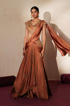 Woman in a metallic mocha  traditional outfit standing againsta beige wall on a red carpet.