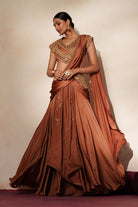 Woman in a metallic mocha  traditional outfit standing againsta beige wall on a red carpet.