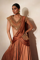 Woman in a metallic mocha  traditional outfit standing againsta beige wall on a red carpet.