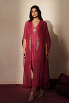 Woman in a mauve pink traditional outfit standing againsta beige wall on a red carpet.