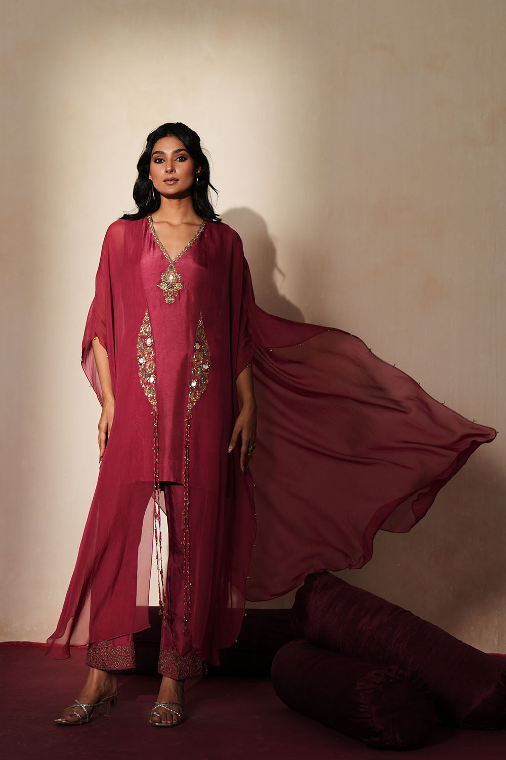 Woman in a mauve pink traditional outfit standing againsta beige wall on a red carpet.