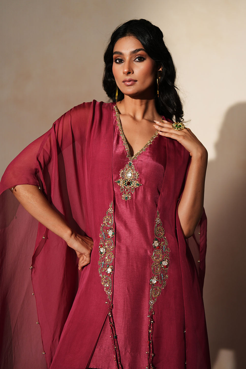 Woman in a mauve pink traditional outfit standing againsta beige wall on a red carpet.