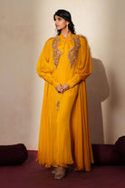 Woman in a golden yellow traditional outfit standing againsta beige wall on a red carpet.