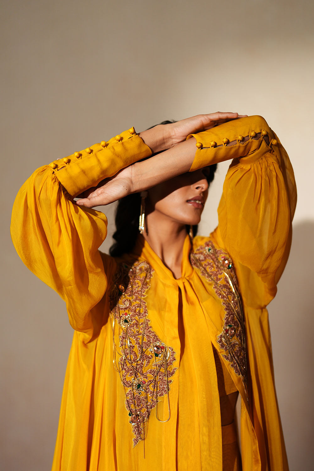 Woman in a golden yellow traditional outfit standing againsta beige wall on a red carpet.