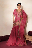 Woman in a mauve pink traditional outfit standing againsta beige wall on a red carpet.