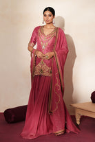 Woman in a mauve pink traditional outfit standing againsta beige wall on a red carpet.