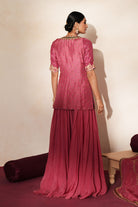 Woman in a mauve pink traditional outfit standing againsta beige wall on a red carpet.