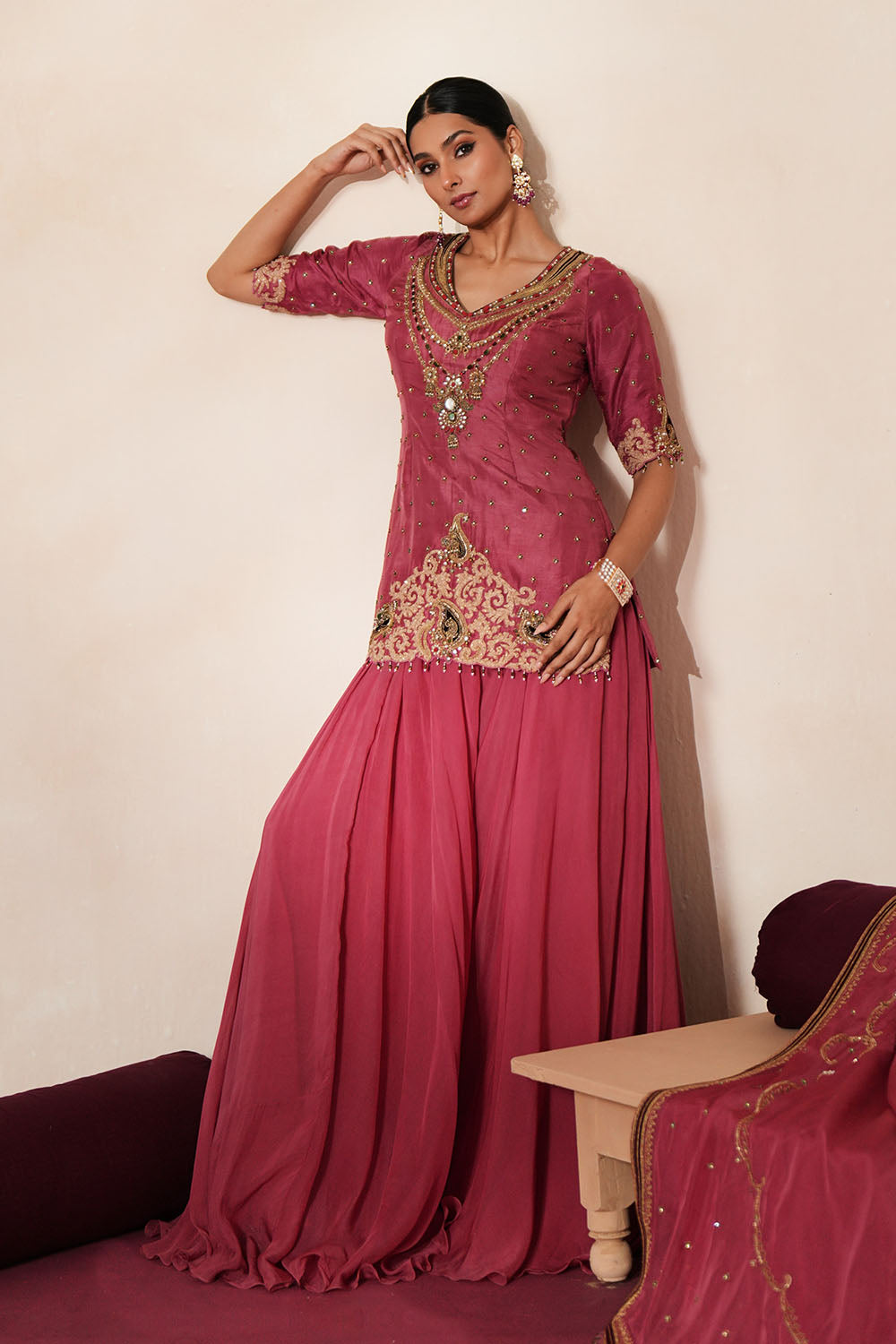 Woman in a mauve pink traditional outfit standing againsta beige wall on a red carpet.