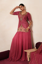 Woman in a mauve pink traditional outfit standing againsta beige wall on a red carpet.