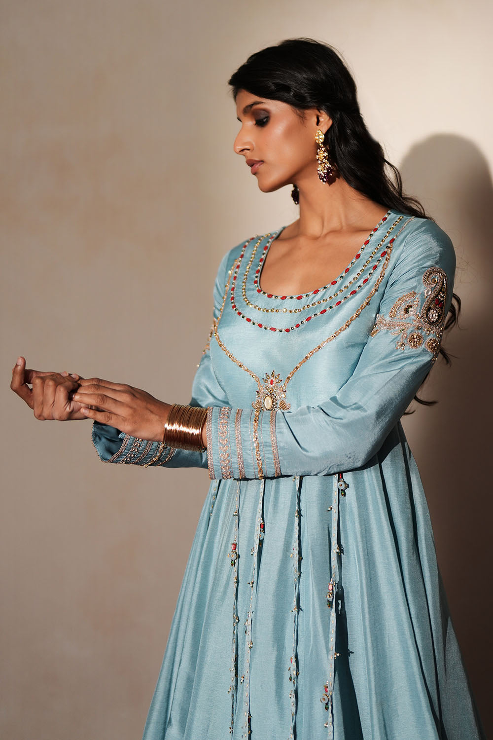 Woman in a pastel blue traditional outfit standing againsta beige wall on a red carpet.