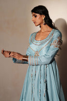 Woman in a pastel blue traditional outfit standing againsta beige wall on a red carpet.