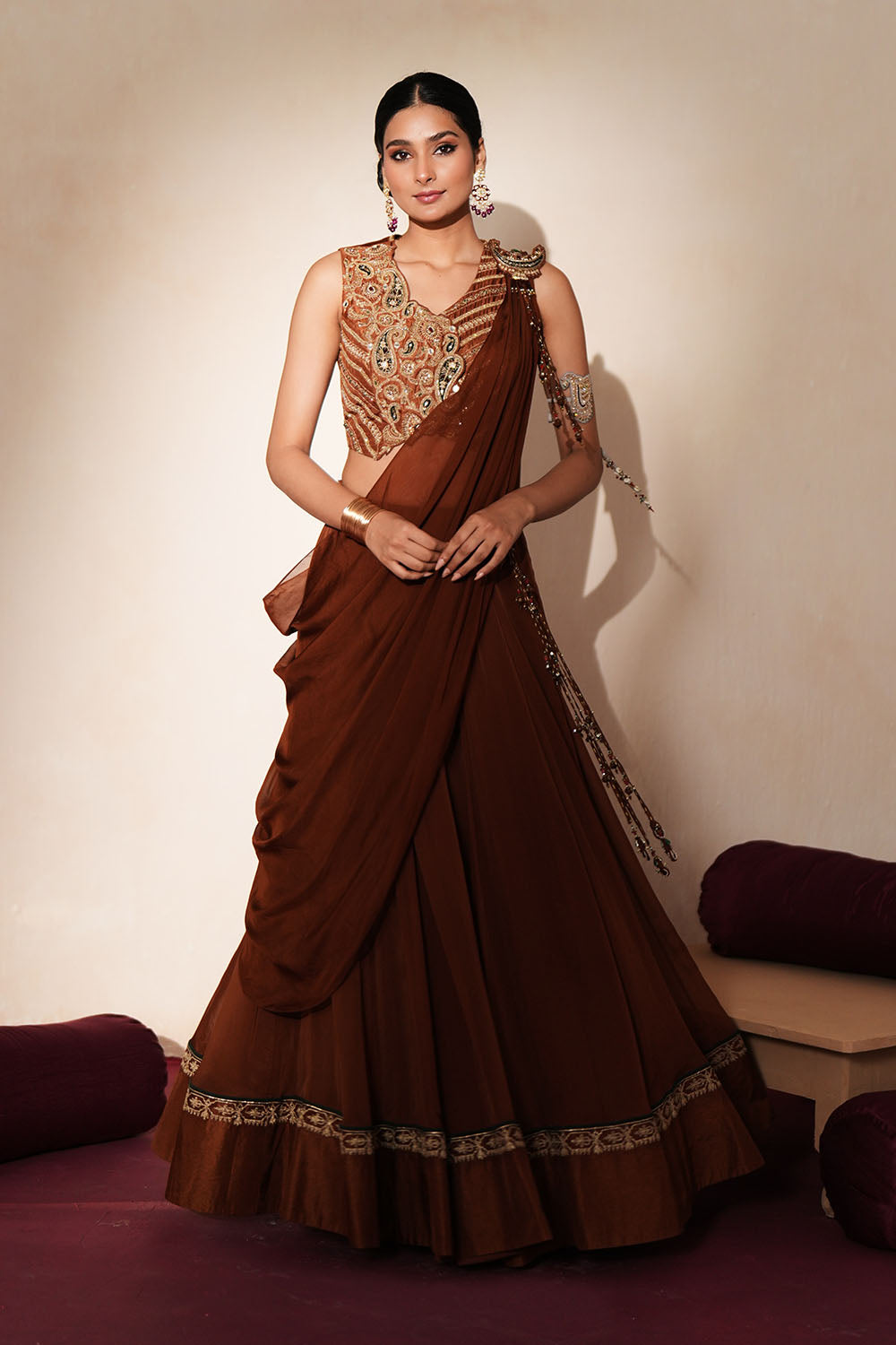 Woman in a mettalic brown traditional outfit standing againsta beige wall on a red carpet.