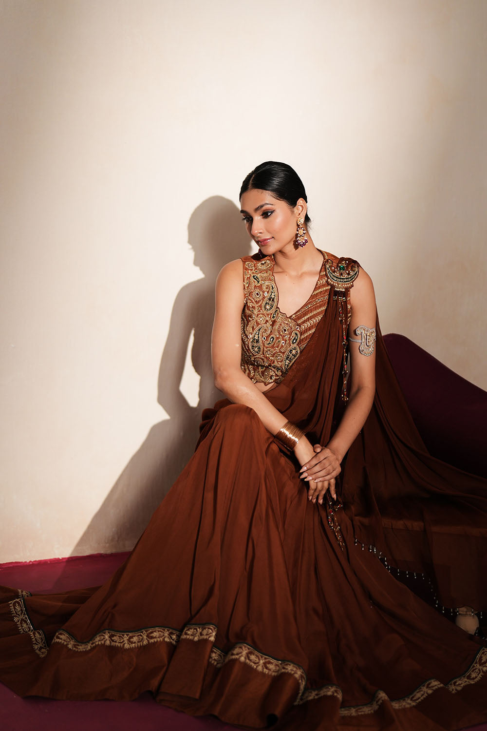 Woman in a mettalic brown traditional outfit standing againsta beige wall on a red carpet.