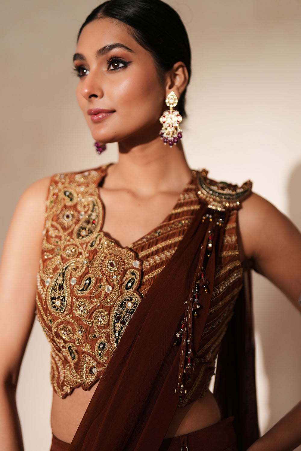 Woman in a mettalic brown traditional outfit standing againsta beige wall on a red carpet.